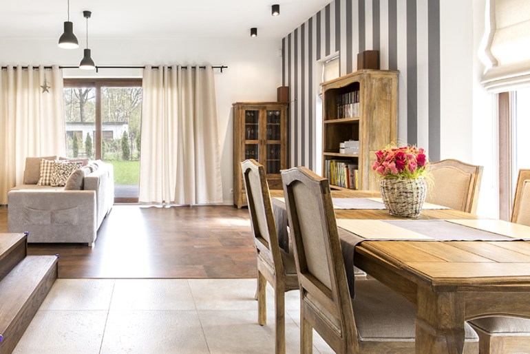 Soggiorno e sala da pranzo luminosi con ampie finestre, tende chiare e arredi in legno
